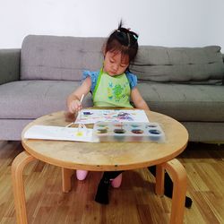 Girl painting while sitting on sofa at home