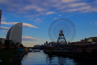 Ferris wheel by river against sky in city
