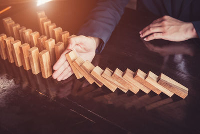 High angle view of man holding falling wooden domino blocks on table