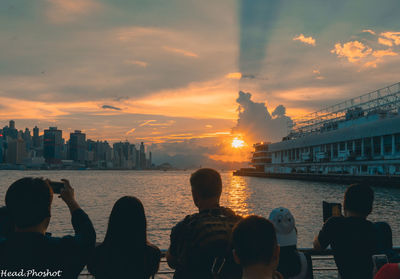 Rear view of people by buildings against sky during sunset