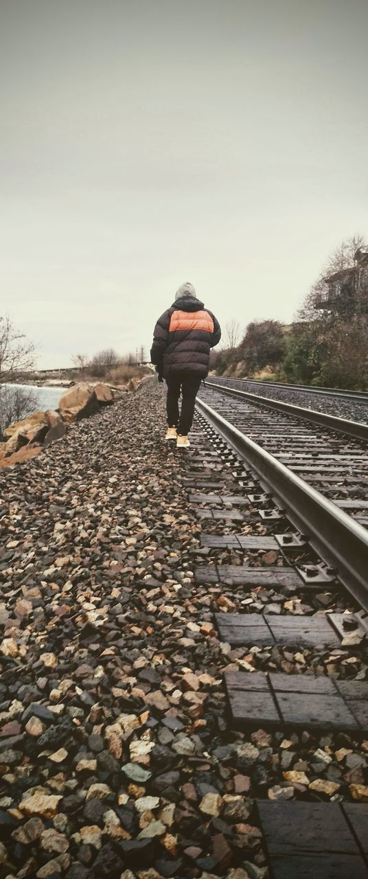 REAR VIEW OF A MAN WALKING ON RAILROAD TRACK