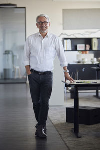 Happy businessman standing with hand in pocket at office