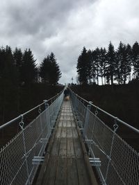 Footbridge amidst trees against sky