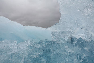 Low angle view of iceberg against cloudy sky