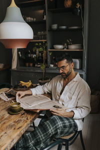 Man reading newspaper while sitting on chair at home