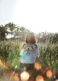 Woman looking away while standing on field against clear sky during sunny day