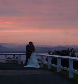 Romantic couple in wedding dress while standing on promenade during sunset