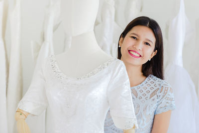 Portrait of smiling young woman standing against white wall