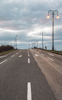 Street lights on road against cloudy sky