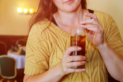 Midsection of mid adult woman holding ice tea in restaurant