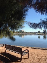 Empty bench by lake against sky