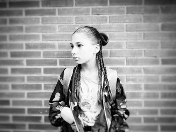 Thoughtful girl standing against brick wall