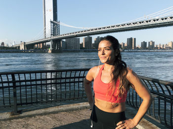 Young woman exercising on footpath against bridge in city