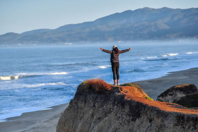 Rear view of man standing on rock by sea against sky