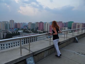 Full length of woman looking at cityscape against cloudy sky