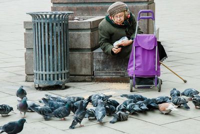 Senior woman feeding pigeons on footpath in city