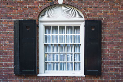 Traditional arched window with black wooden shutters on a red brick wall of an apartment building