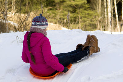 Rear view of teenage girl sliding with sled on snow covered field