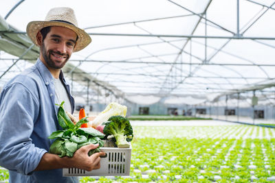 Portrait of smiling man holding basket with vegetable standing at vegetable farm