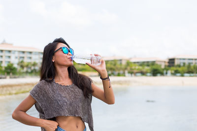 Young woman standing at beach against sky