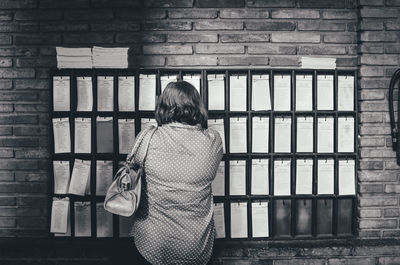 Rear view of woman standing against brick wall