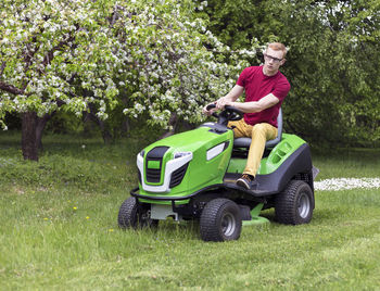 Young man riding lawn mower at grassy field