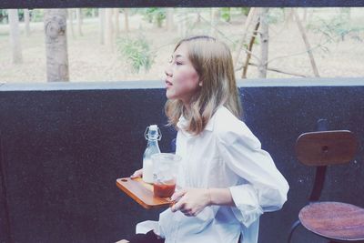 Woman holding drinks while sitting outdoors