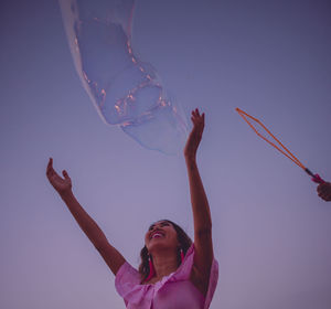 Low angle view of cheerful woman playing with bubble against sky during sunset