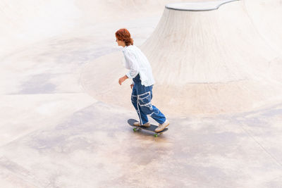 From above full body side view of active female in casual wear riding skateboard in skate park with ramp on summer day