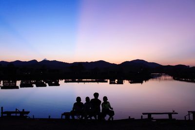 Silhouette people sitting by lake against clear sky