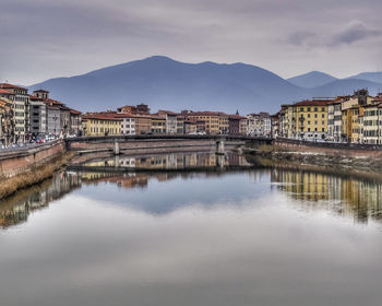 Arch bridge over river by buildings in city against sky