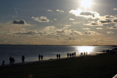 Silhouette people on beach against sky during sunset