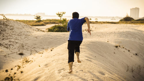 Rear view of man running at beach against sky during sunset