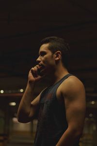 Side view of young man using phone while standing in basement