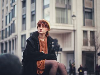 Young woman looking away while sitting in city