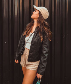 Young woman looking away while standing with mask against wall