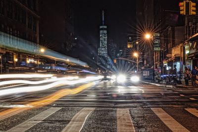 Light trails on road against illuminated one world trade center at night