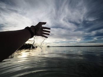 Close-up of hand on sea against sky