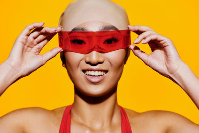 Close-up portrait of young woman wearing sunglasses against yellow background