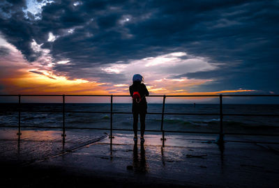 Rear view of man looking at sea against sky during sunset