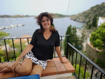 Portrait of smiling young woman standing by railing against lake