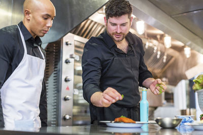 Male chefs garnishing food at kitchen counter in restaurant