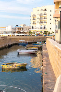 Boats moored in river by buildings in city against sky