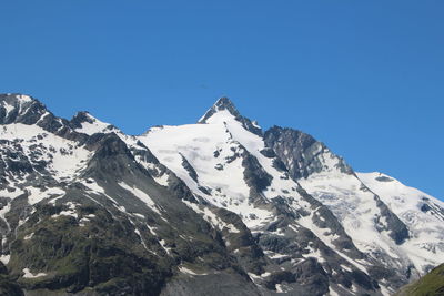 Low angle view of snowcapped mountains against clear blue sky