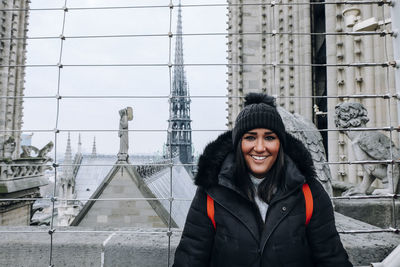 Portrait of smiling young woman standing against buildings during winter