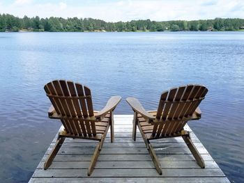 Empty chairs on pier by lake against sky