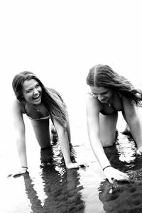 Portrait of smiling young woman standing at beach against clear sky