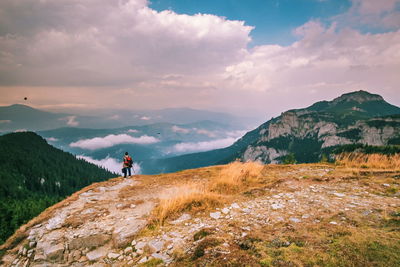 Rear view of hiker standing on mountains against cloudy sky