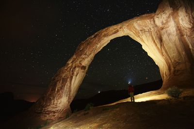 Man standing by illuminated corona arch against star field