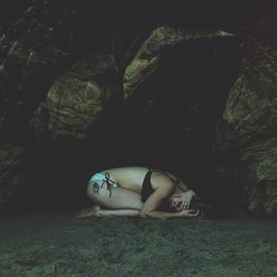 Full length of sensuous woman in bikini kneeling by cave at beach